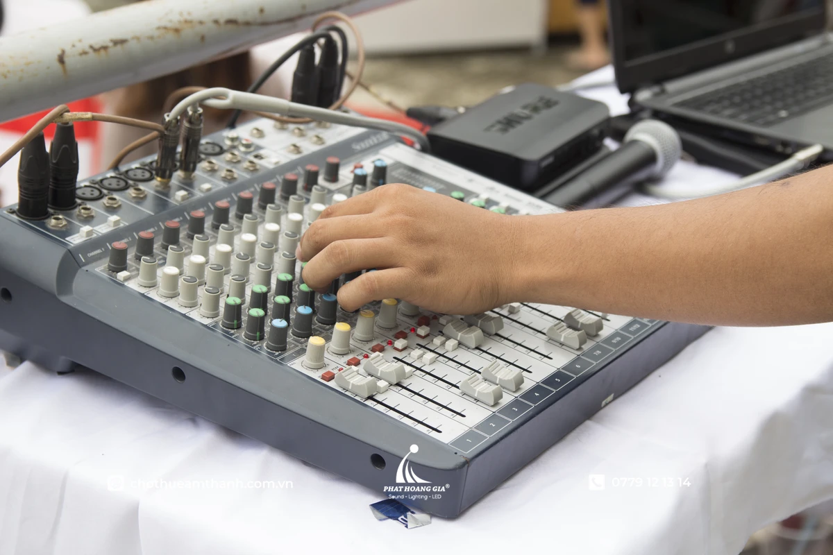 Kỹ thuật viên đang điều chỉnh các kênh tín hiệu trên bàn mixer để cân bằng tần số và tối ưu chất lượng âm thanh cho sự kiện