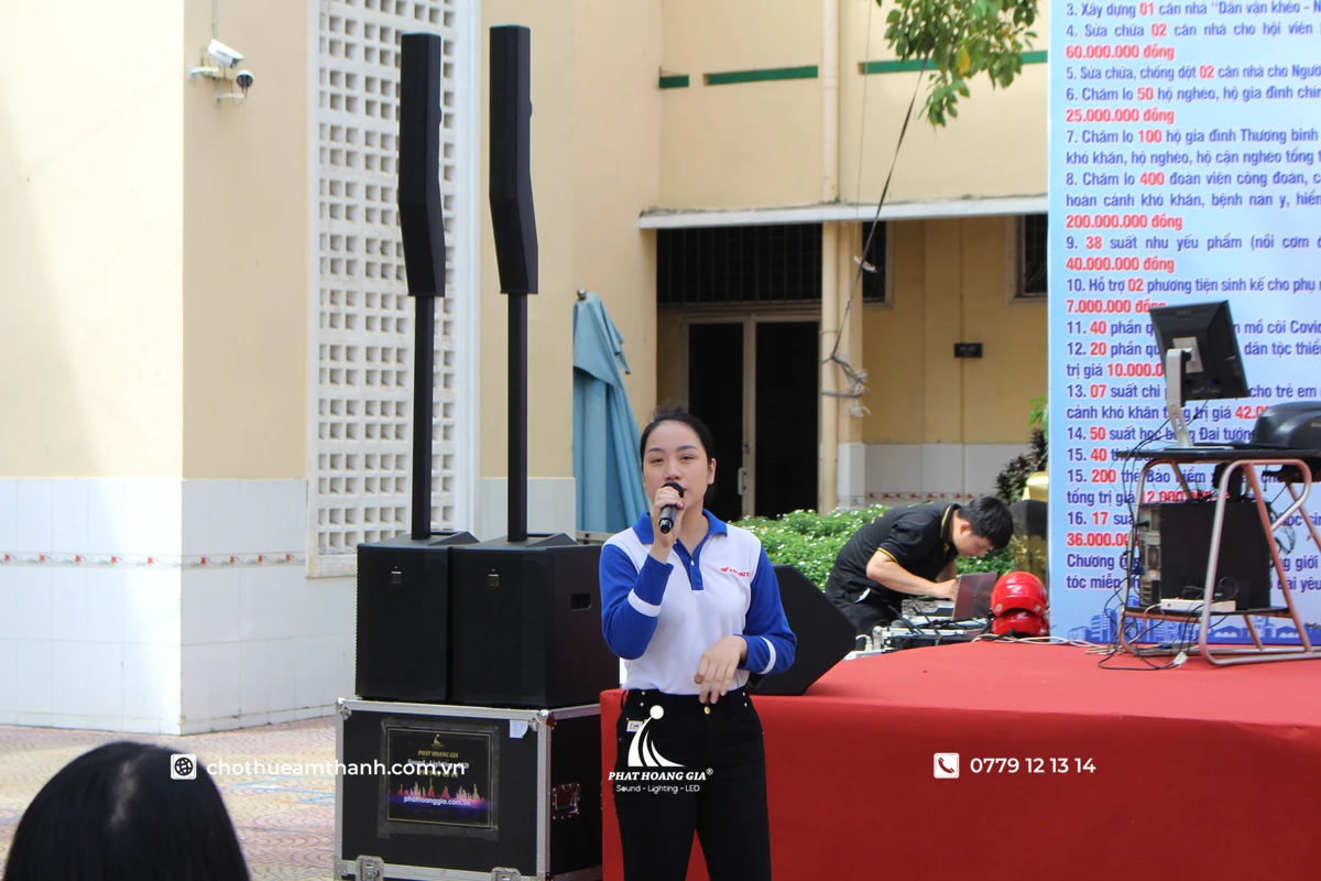 MC đang phát biểu trên sân khấu trong khi đội ngũ kỹ thuật vận hành hệ thống âm thanh sự kiện để đảm bảo chất lượng âm thanh ổn định cho khán giả